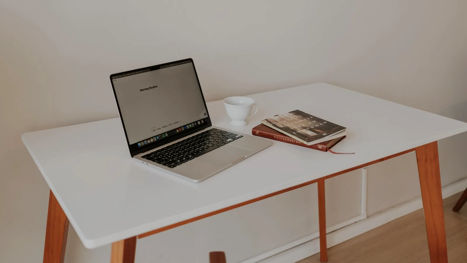 A laptop, a coffee cup and books on a white desk