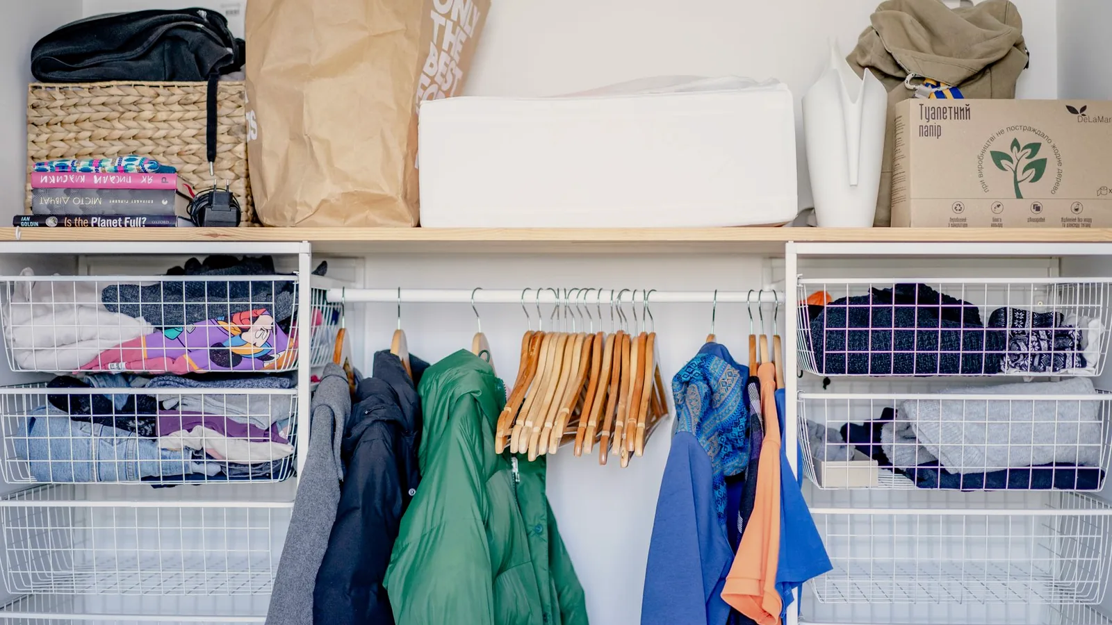 An open wardrobe with hung clothes and woven storage baskets