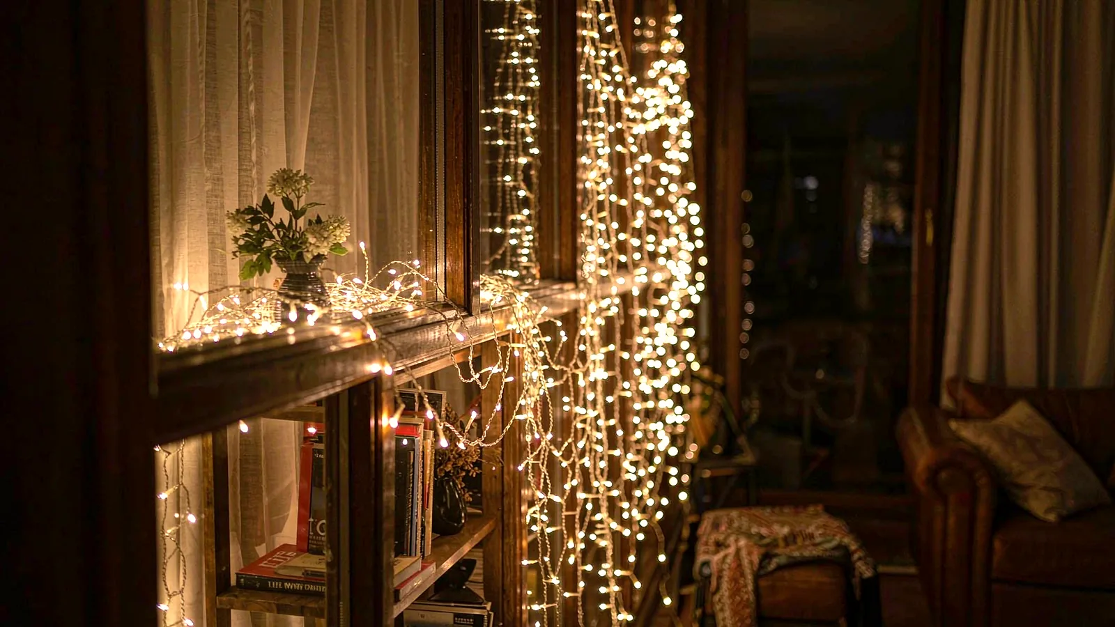 Warm string lights draped along a window and bookshelf in a dim room