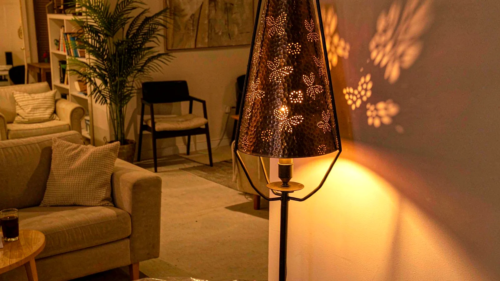 A glowing metal lamp shade on a floor lamp against a pale wall