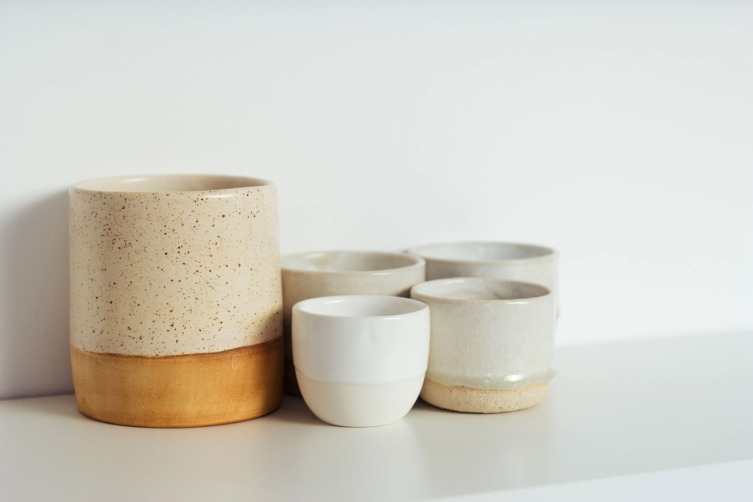Neutral ceramic cups and bowls on a shelf; gift-category context.